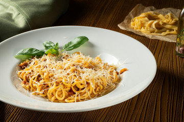 Bolognese pasta with red sauce, parmesan and minced meat. Italian spaghetti with meat in a white plate on a wooden background.