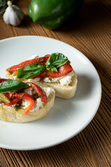 bruschetta with bell pepper, basil, pesto sauce and Cream cheese on a white plate on a wooden background. Italian restaurant. Top view food photo