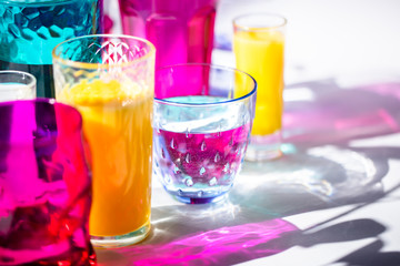 Glass goblets create wonderful coloured shadows on a solar table. The shadow of sunlight reflect to glass of pink and yellow, emerald colors