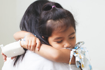 Sick asian child girl who have IV solution bandaged hugging her mother with love in the hospital