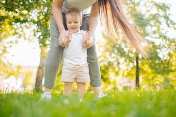 Happy smiling child boy makes first step in park, mom helps