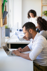 Serious male employee working on project in office. Man and women in casual sitting and standing at table and using laptops. Workspace concept