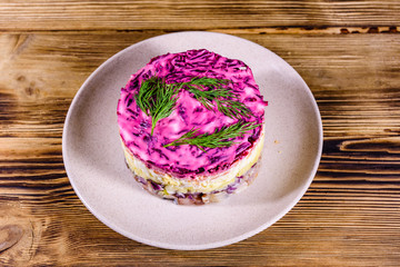 Ceramic plate with russian traditional new year salad herring under fur coat (shuba) and on rustic wooden table