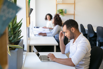 Excited male professional looking at laptop screen in surprise. Man and women in casual sitting at...