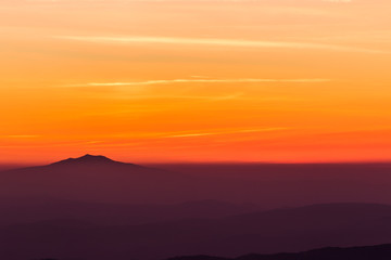 Obraz premium Beautifully colored sky at sunset, with mountains layers and mist between them