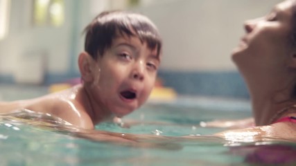 A young brunette woman teaches her child to dive into the water, swimming in the sports pool. Mother and son swim in the pool, the child dives into the water while mother is holding him and making