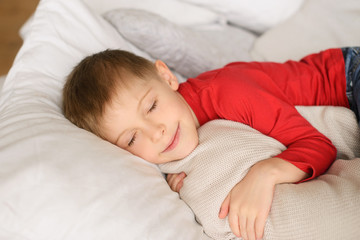 cute blond boy in red jersey sleeps among  white pillows, blankets and hugs