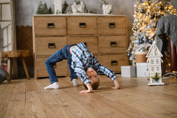 boy stands in an acrobatic pose on  wooden floor, against background of Christmas tree, glowing...