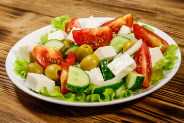 Greek salad with fresh vegetables, feta cheese and green olives on wooden table