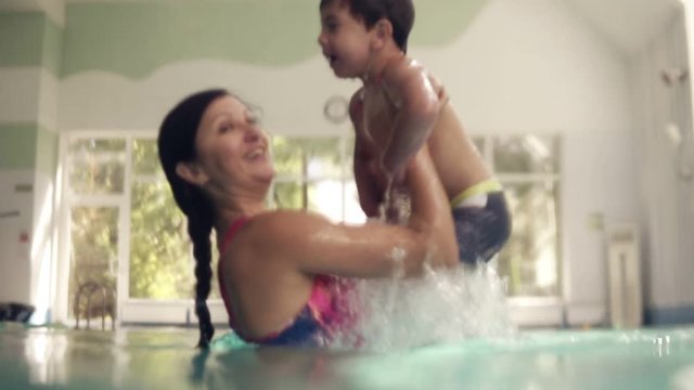 Cute brunette toddler is diving under the water in the swimming pool and swimming there until his mother helps him to get out. An underwater shot