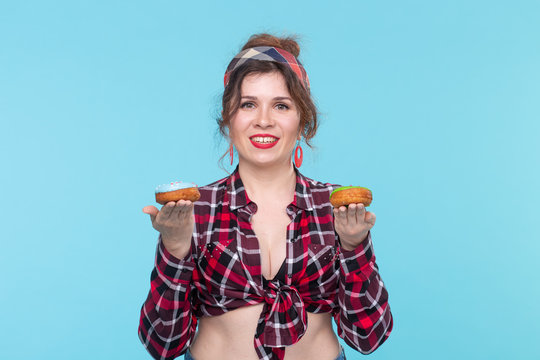 Positive young pin-up girl model holding in hands multicolored donuts posing on a blue background. Cooking concept for desserts and sweets.