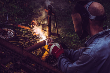 Man using welding machine stick to cut melt iron metal construction outdoors, wearing protective...