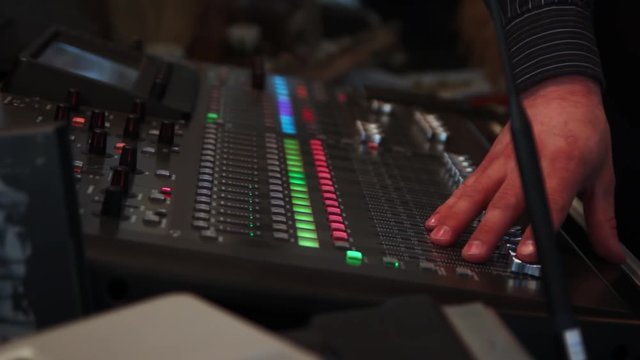 Handheld shot of a DJ handling a dj pult. Turning some levels down.