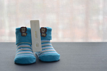 Positive pregnancy test and baby shoes on black background. Concept of pregnancy.