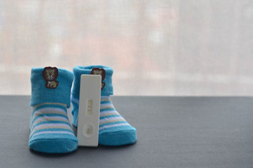 Positive pregnancy test and baby shoes on black background. Concept of pregnancy.