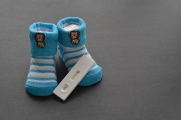 Positive pregnancy test and baby shoes on black background. Concept of pregnancy.