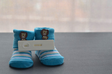 Positive pregnancy test and baby shoes on black background. Concept of pregnancy.