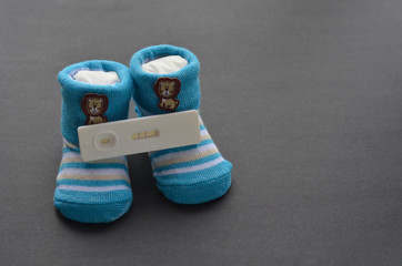 Positive pregnancy test and baby shoes on black background. Concept of pregnancy.