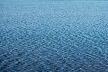 Blurred water background. Texture of small ripples on the water. Saturated blue shades with a light gradient.