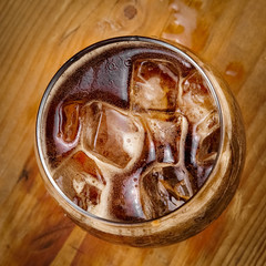 Glass of cola with ice on wood, top view