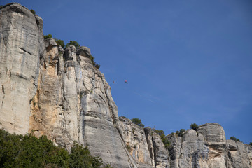 The vertical cliffs of the stone of Bismantova with tightrope walkers and the blue sky in the background.