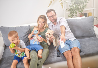 Young parents watching TV with baby boy and a dog.