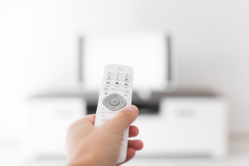 Hand holding TV remote controller with a modern television set.