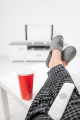 Man drinking soda juice and looking at TV with legs on the table in living room.