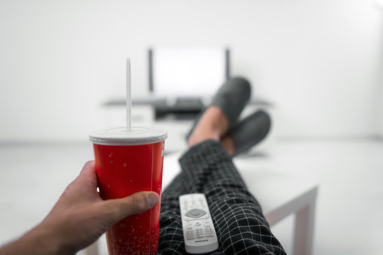 Man drinking soda juice and looking at TV with legs on the table in living room.