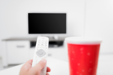 Hand holding TV remote controller with a soda juice and TV.