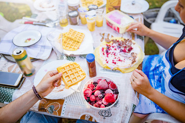 People making a picnic with sweet waffle and pancaces in the garden.