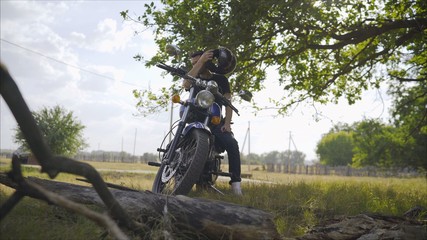 A man on a motorbike against the sea. Motorcyclist stands under a tree. Motorcyclist with a motorcycle in the summer in a clearing.