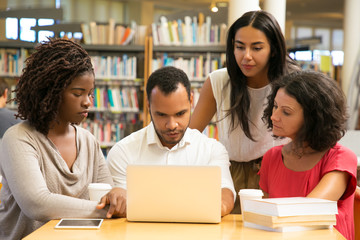 Serious mature students working with laptop at public library. Focused friends working over new...