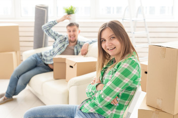 Fototapeta na wymiar Positive smiling young girl sitting against her laughing blurred husband in a new living room while moving to a new home. The concept of joy from the possibility of finding new housing.