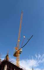 Closeup of yellow crane under working at construction site with blue sky background. 