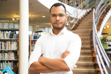 Confident guy with crossed arms standing in front of stairs. Front view of smiling African American...