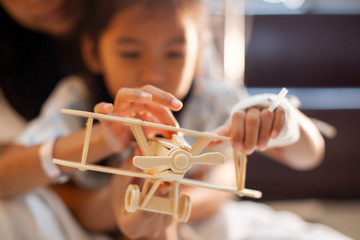 Sick asian child girl playing with toy wooden airplane with her mother while stay in the hospital with fun