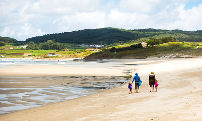 Happy young family is walking on sandy beach and ocean. 