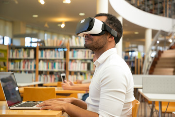 Adult male student training with VR headset in library. Man wearing virtual reality glasses,...