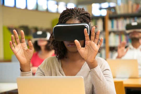 Multiracial group of students using VR gadgets during class. Young black woman in virtual reality headset sitting at desk with laptop and touching air. Devices for education concept