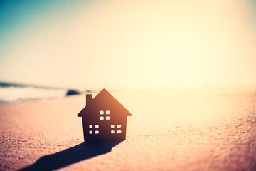 Small home model on sunset beach sand texture background.