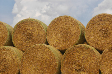 stack of straw bales - close up view of round straw bales stacked on top of each other, blue sky with white clouds