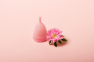 Menstrual cup and flower on a pink background. The concept of menstruation. Flat lay, top