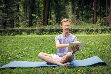 Young attractive white man learns how to meditate in the park  smiles and using a map-case.