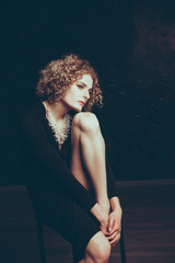 Young androgyne male in the image of a girl with an afro hair and makeup posing sitting embraced...