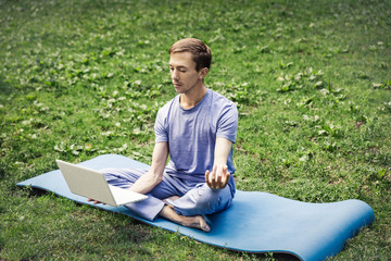 Young attractive white man learns how to meditate in the park  using a tablet.