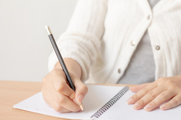 Female hand with pencil writing on blank paper notebook.Woman with white sweater.