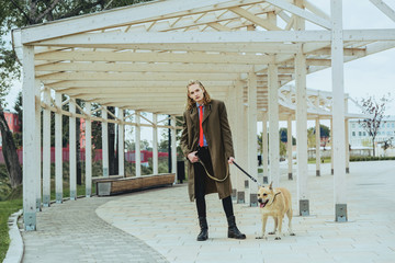 A handsome young guy in a khaki and berets military coat looks on a big  dog. 