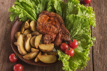 pork steak with fried potatoes on lettuce leaves with cherry tomatoes