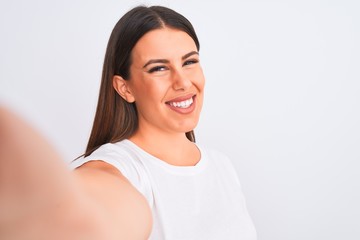 Beautiful young woman taking a selfie photo using smartphone over white background with a happy face standing and smiling with a confident smile showing teeth